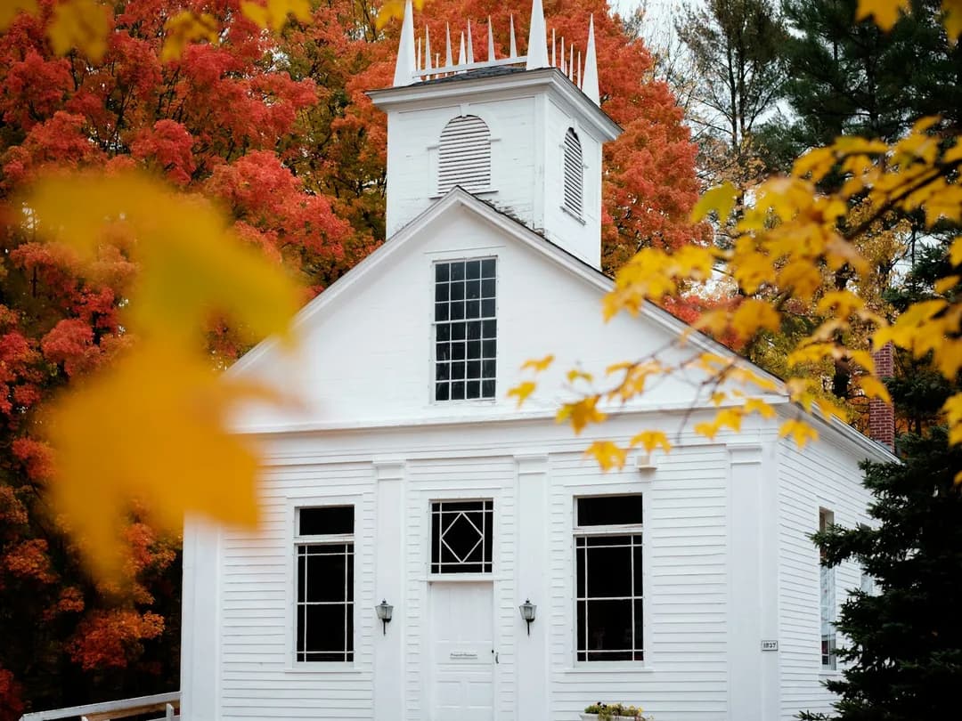 A classic white New England building surrounded by peak fall maples