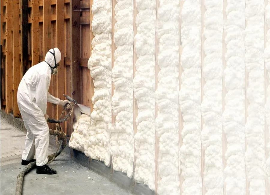 Technician spraying closed-cell foam across framed wall cavities